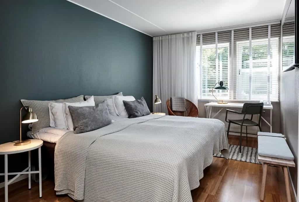 Bedroom at Aspenäs Herrgård with dark teal accent wall, white bedding, and wooden floor.
