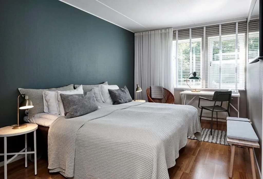 Bedroom at Aspenäs Herrgård with dark teal accent wall, white bedding, and wooden floor.