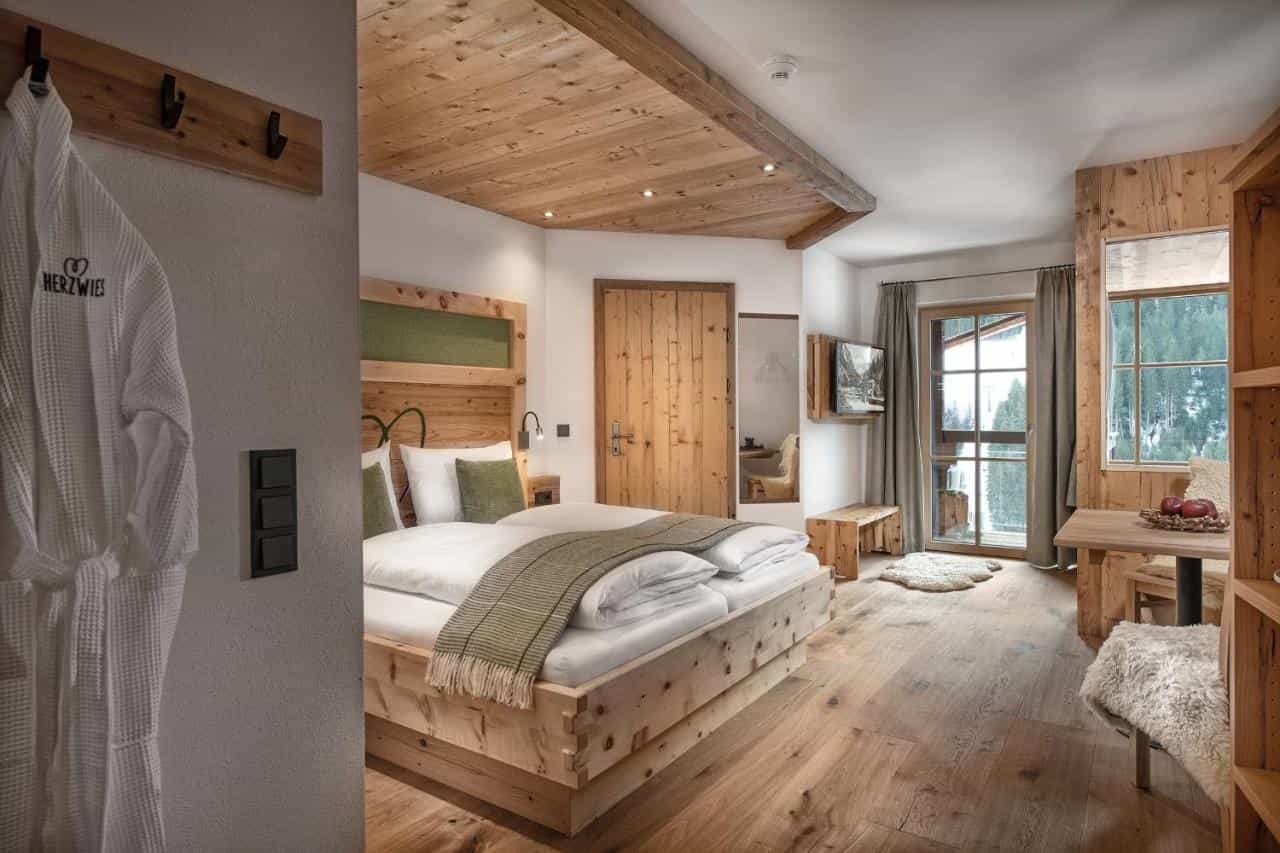 Cozy hotel room with rustic wood paneling, white bedding, and a view of snow-covered trees.