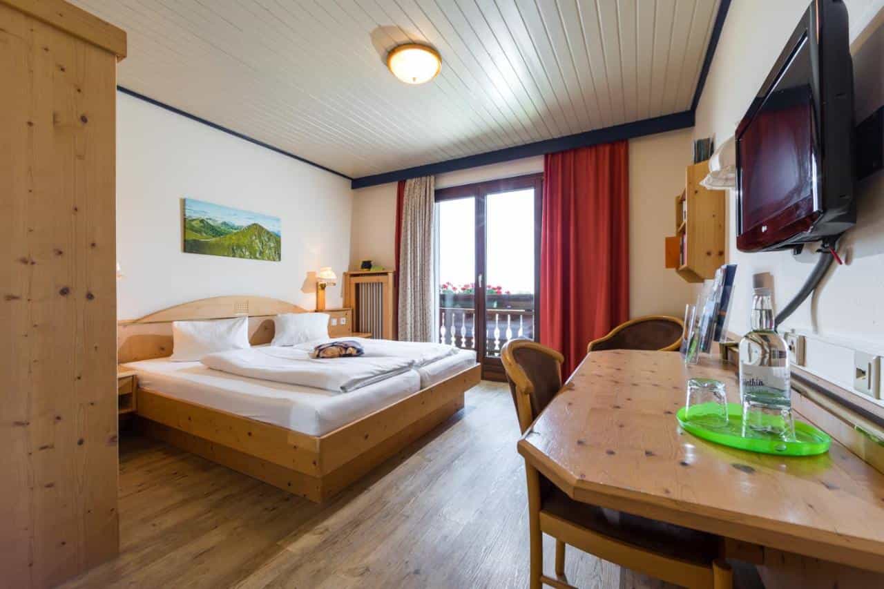 Heidi Hotel Falkertsee room with wooden bed, desk, and balcony view of mountains.