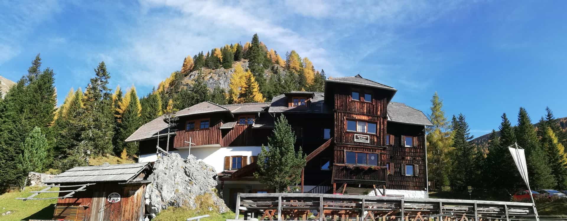 Erlacherhaus wooden mountain lodge nestled against a hillside with autumn trees under blue sky.
