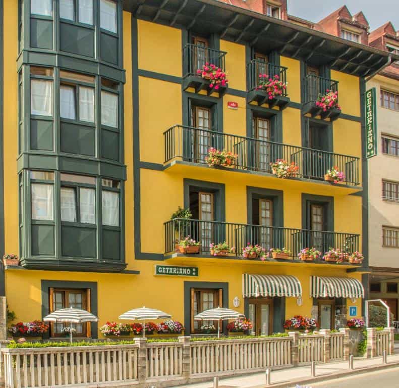 Yellow building with dark green trim, balconies with flowers, and striped awnings in Getariano.