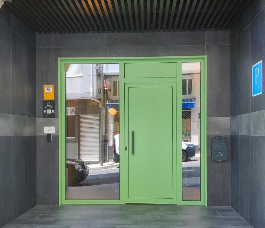 Entrance with bright green door and glass panels set in dark gray tiled wall, reflecting a street.