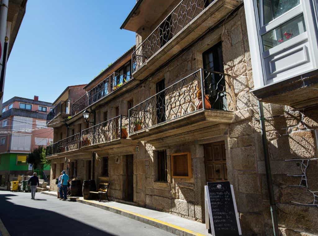 Stone building with wrought iron balconies on a sunny street in a rustic German pension setting.