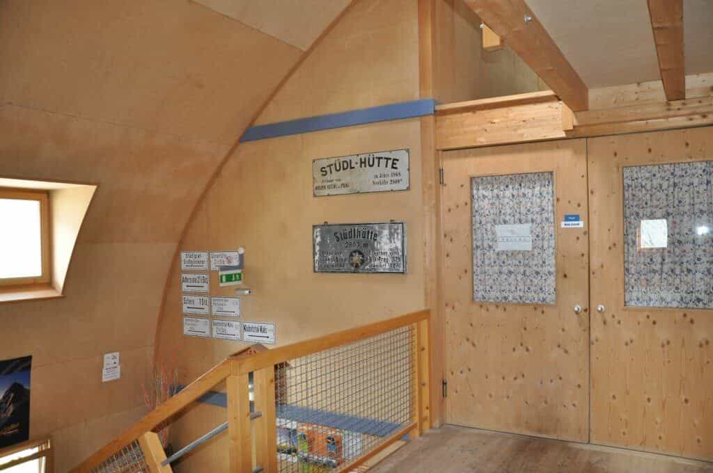 Interior hallway of Stüdlhütte with wooden walls, signs, and a staircase railing.