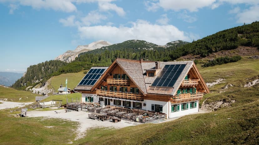 Rifugio Fodara Vedla mountain hut with solar panels in grassy alpine setting under blue sky.