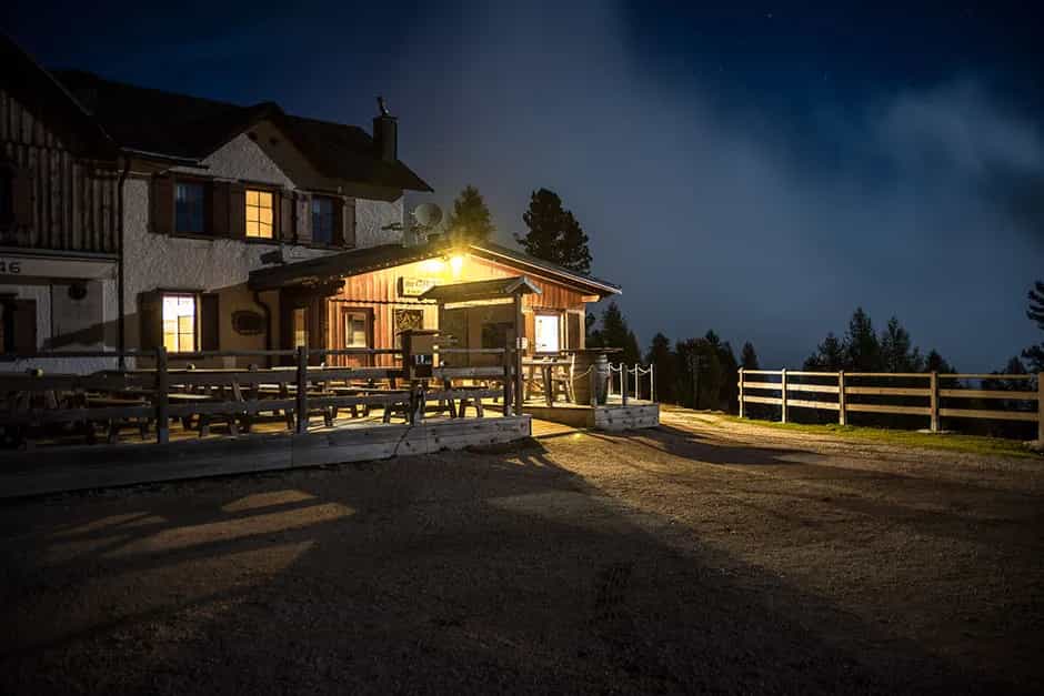 Rifugio Croda da Lago mountain hut illuminated at night with an outdoor deck and dark sky.
