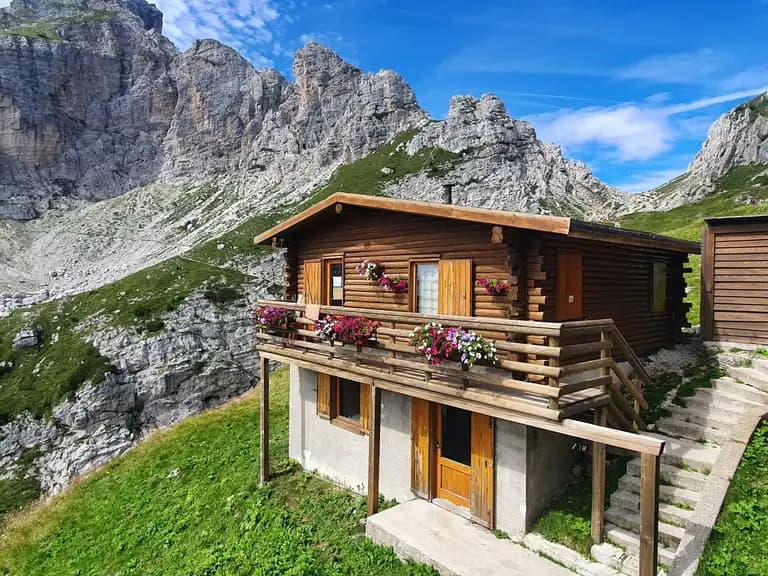 Rifugio Adolfo Sonino al Coldai log cabin set against steep, rocky alpine mountainsides.
