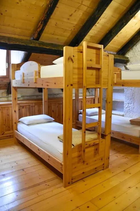 Wooden bunk beds in a rustic room with wood plank walls and sloped ceiling, Malga Pramper