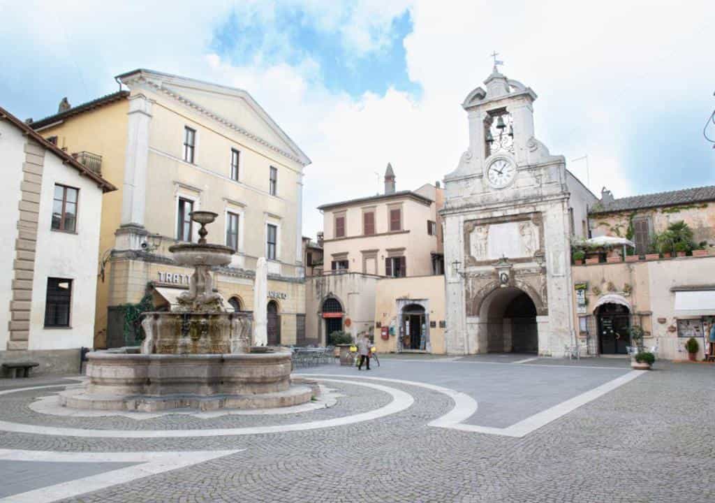 Stone fountain in town square with clock tower archway and surrounding historic buildings