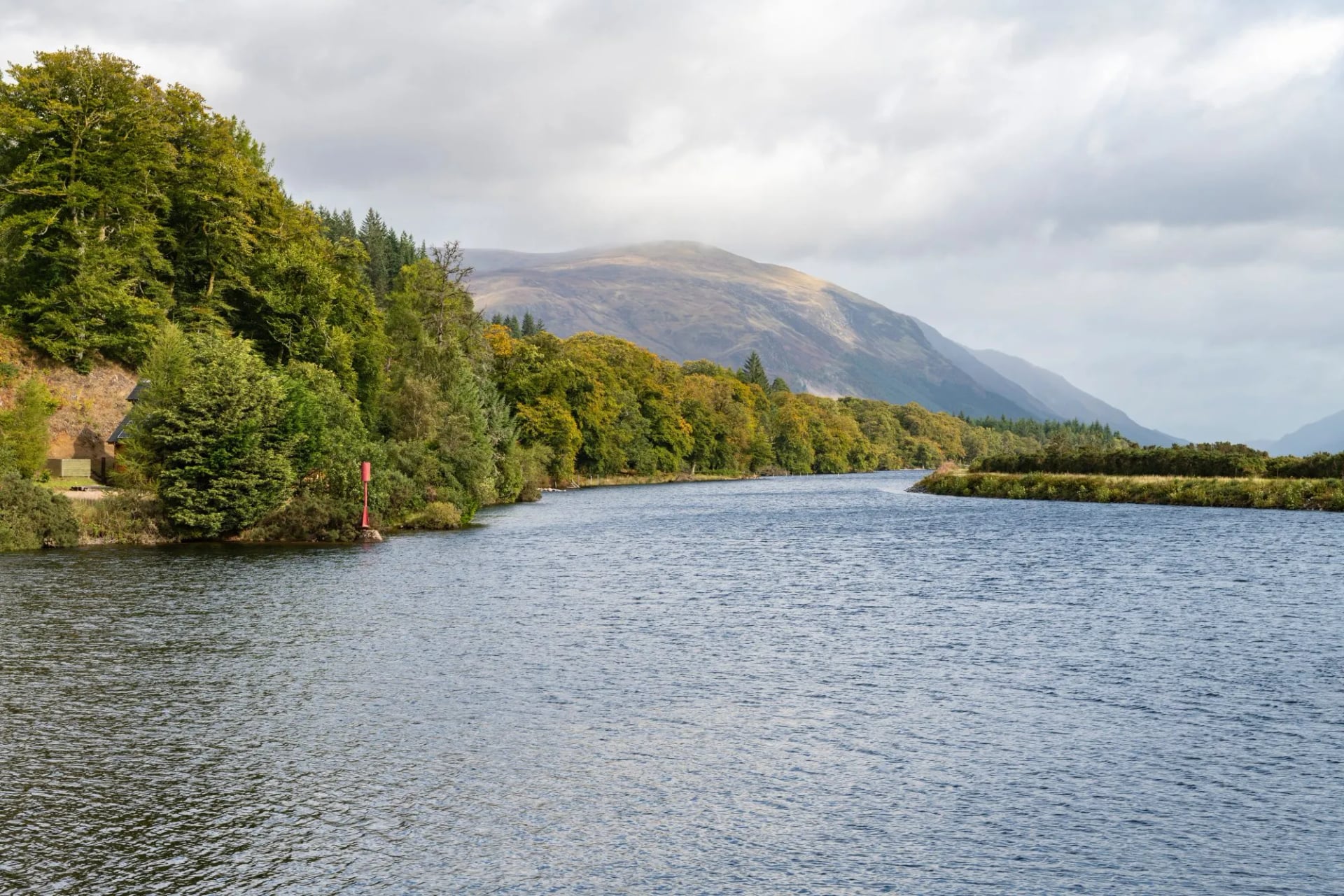 The Caledonian Canal running between wooded banks below a Highland hill