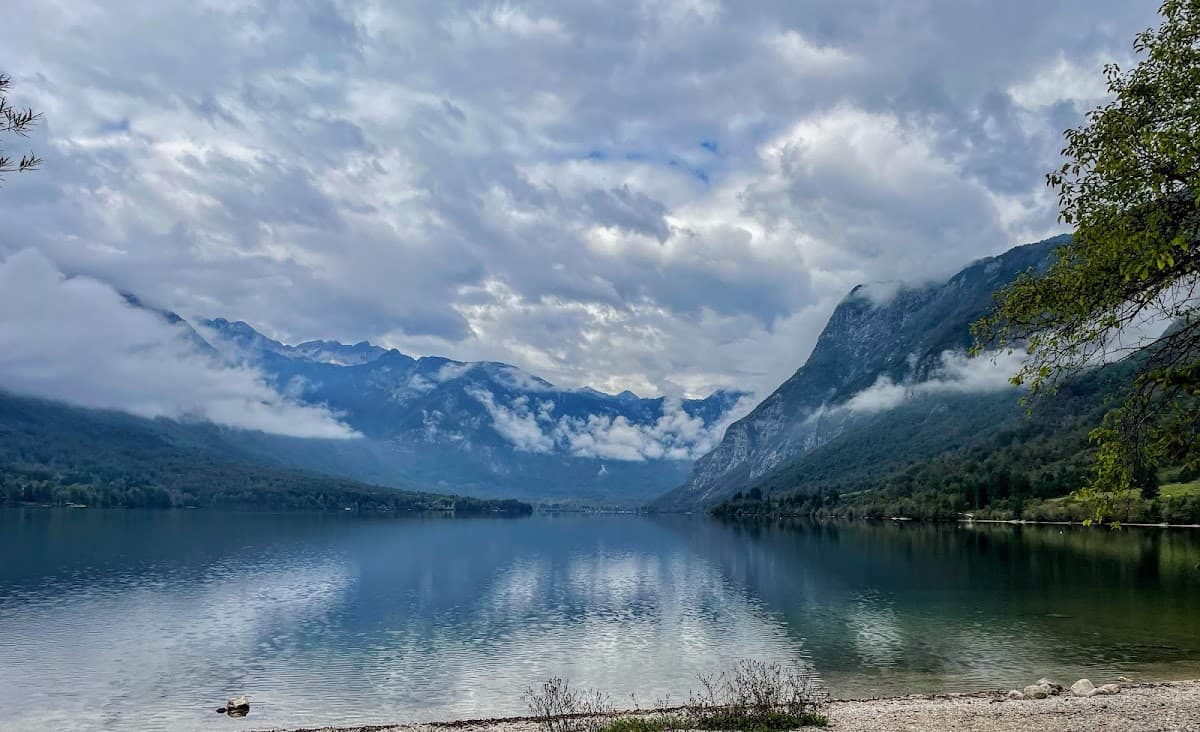 Mountain lake reflecting cloudy sky with fog rolling over forested slopes and peaks