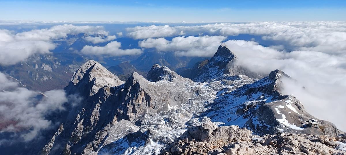 Rocky mountain peaks with snow patches above the clouds under a clear blue sky