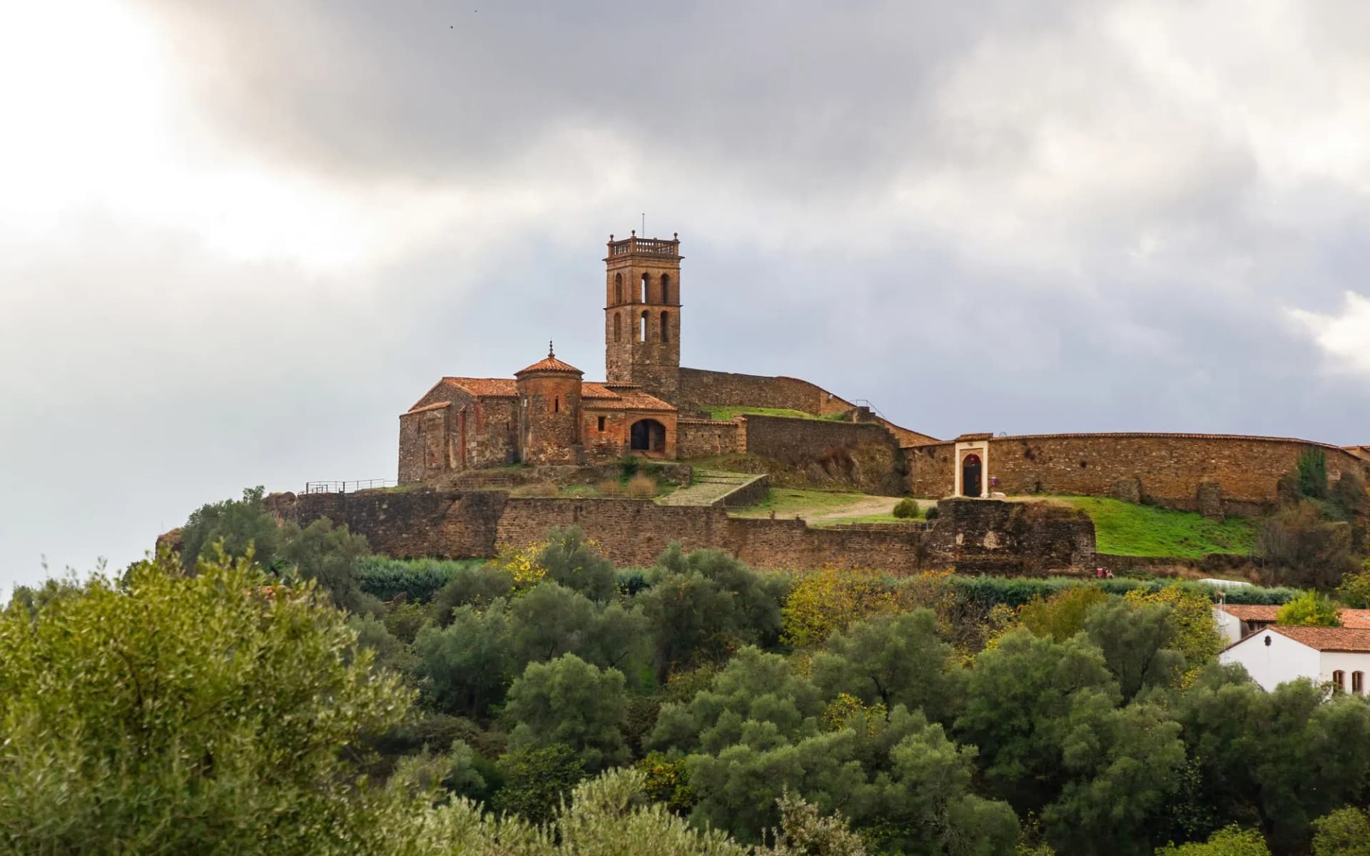 Almonaster la Real Mosque ruins with tower atop a hill over green trees in Huelva, Andalusia, Spain.