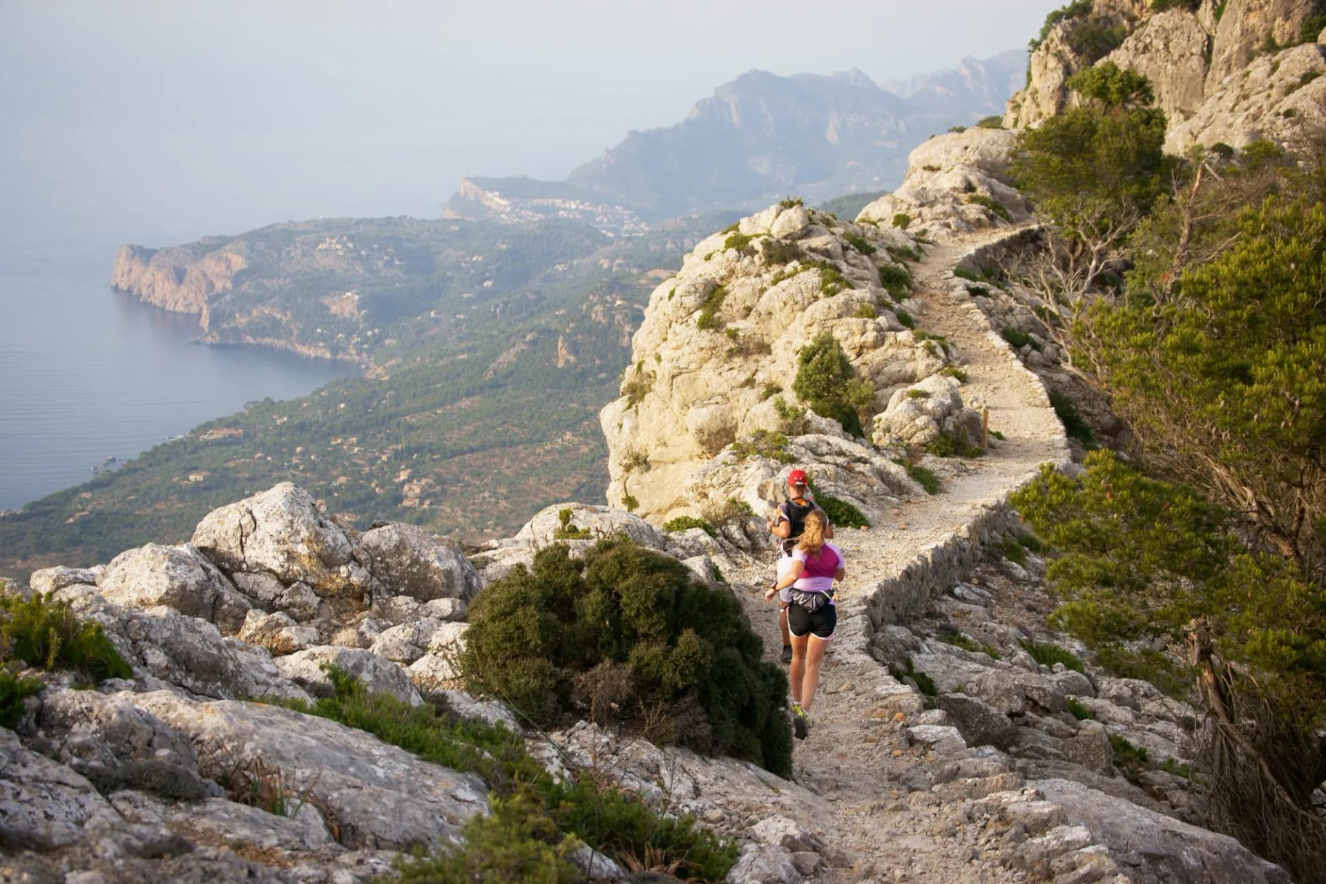 Trail runners on rocky path above Mediterranean coast, Valldemossa, Mallorca