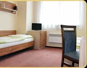 Simple hotel room interior with wooden bed frame, small television, and window light.