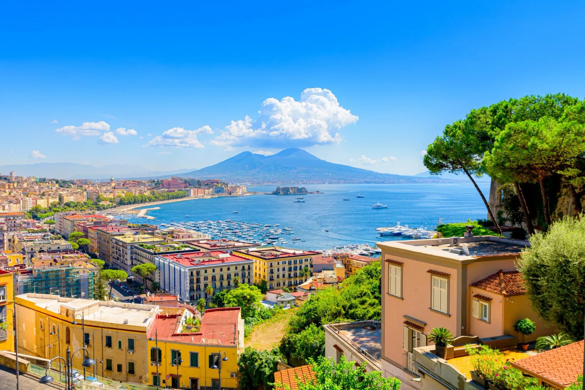 Naples, Italy. View of the Gulf of Naples from the Posillipo hill with Mount Vesuvius far in the background and some pine trees in foreground. August 31, 2021.