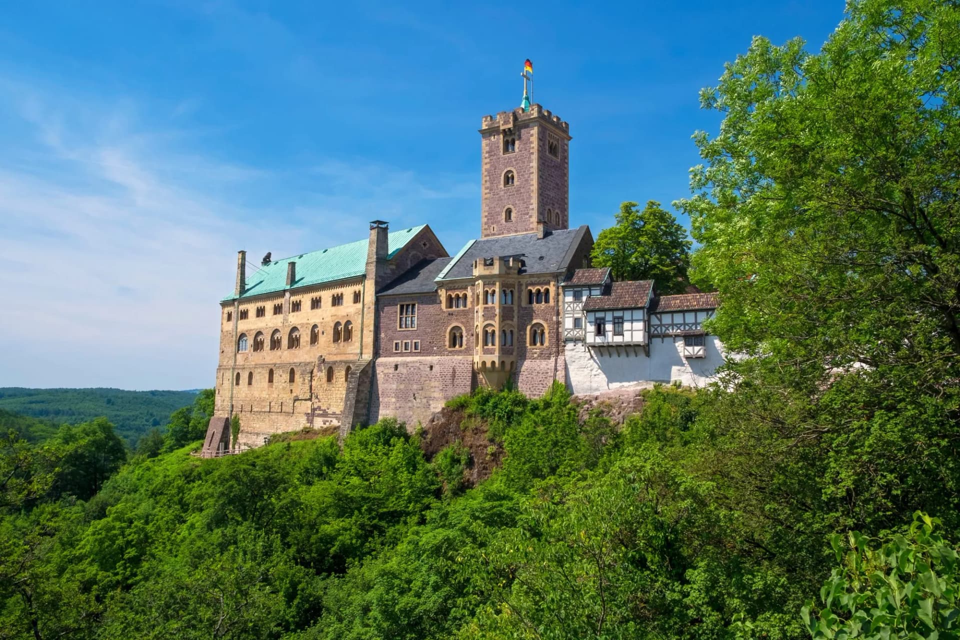 Wartburg Castle on a lush green hill under a bright blue sky.