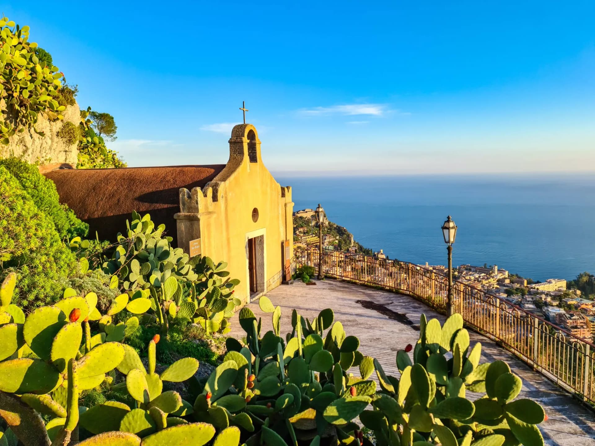 Chiesa di San Biagio of Castelmola with panoramic view on coastline of Ionian Mediterranean sea near Taormina, Sicily, Italy, Europe, EU. A field of cactus around the church at sunset golden hour time
