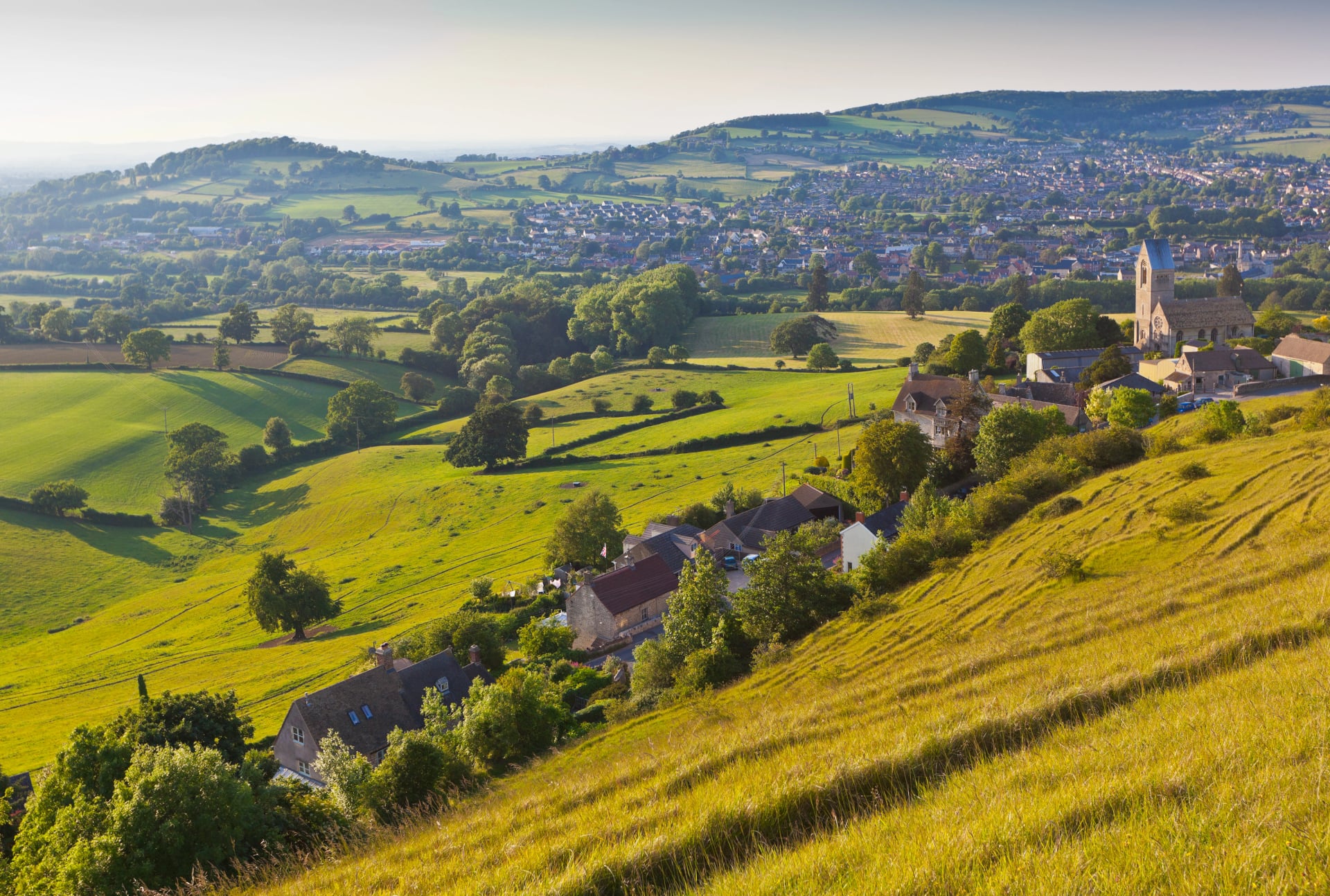 Green hillside above a valley village in the Cotswolds