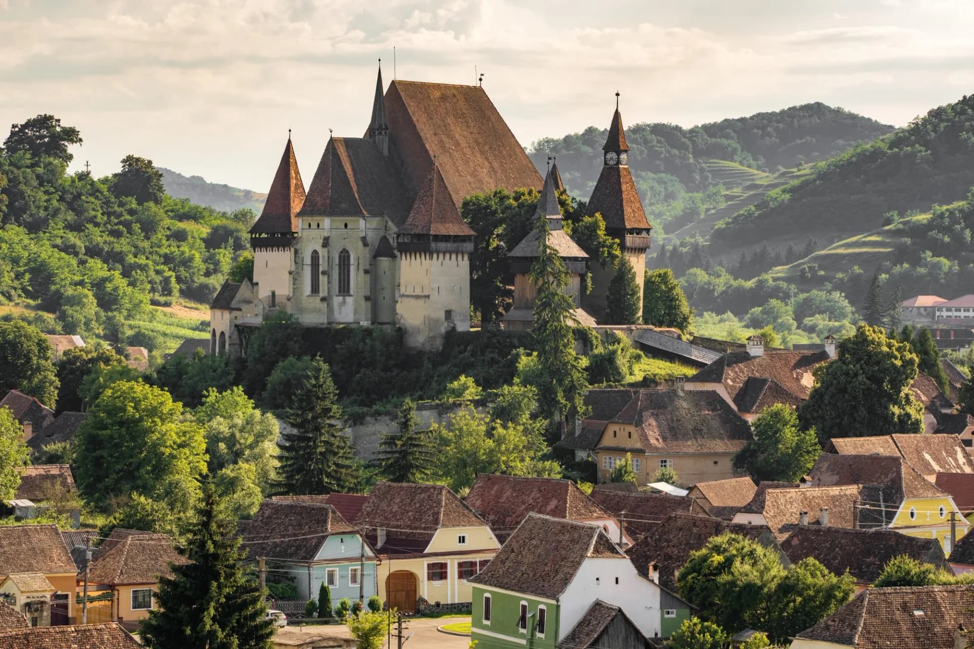 Fortified Saxon church above village houses in Biertan, Transylvania, Romania, surrounded by green hills.