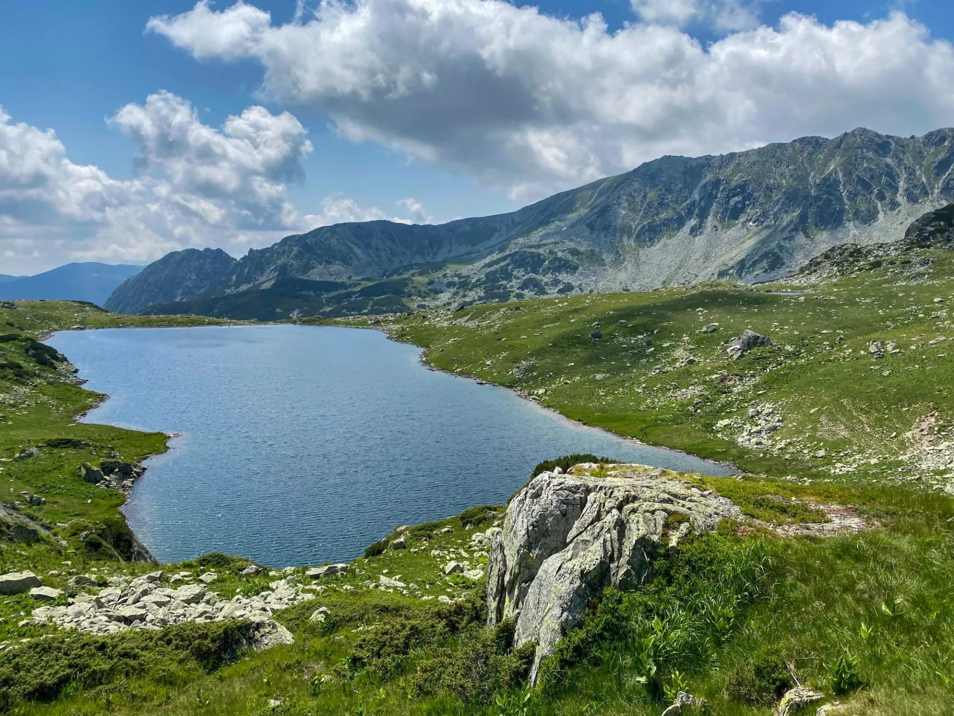 Bucura Lake nestled in green alpine landscape with rocky mountains under blue cloudy sky