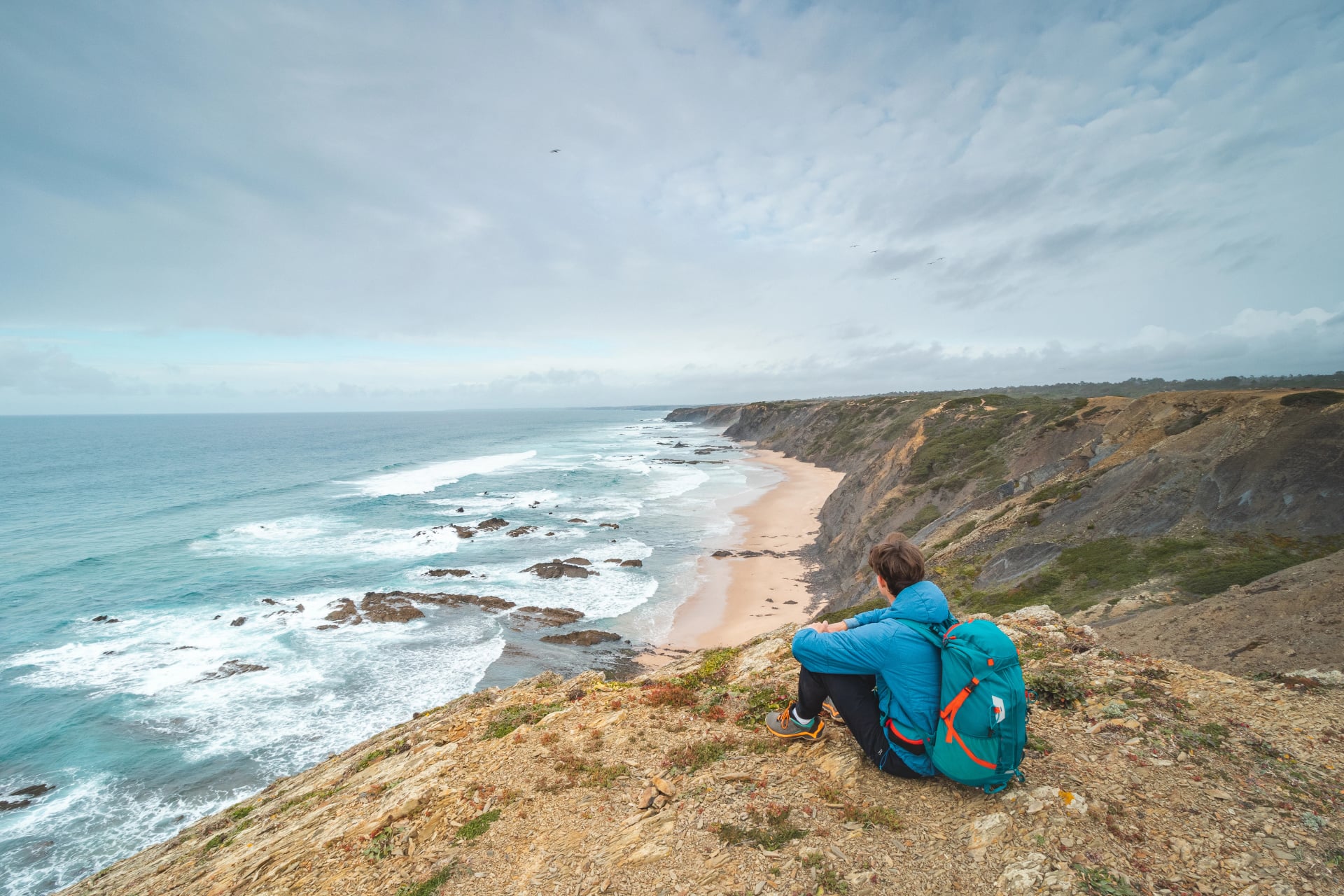 Young man sits above the famous Praia da Carreagem beach in southwest Portugal, near the town of Aljezur in the Odemira region. Wandering along the Fisherman Trail