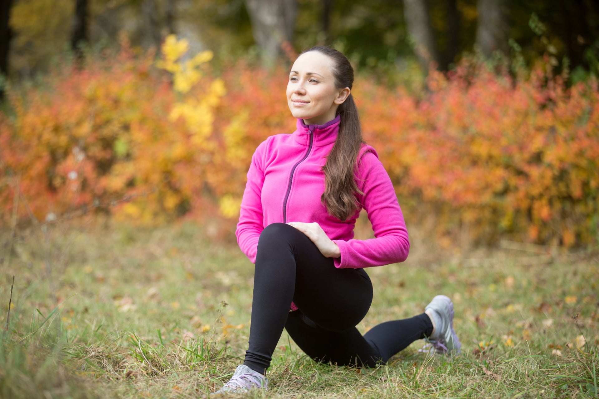 Portrait of sporty beautiful happy young woman practicing yoga, standing in low lunge exercise, warming up, stretching before morning running routine, working out outdoor on autumn day in sportswear