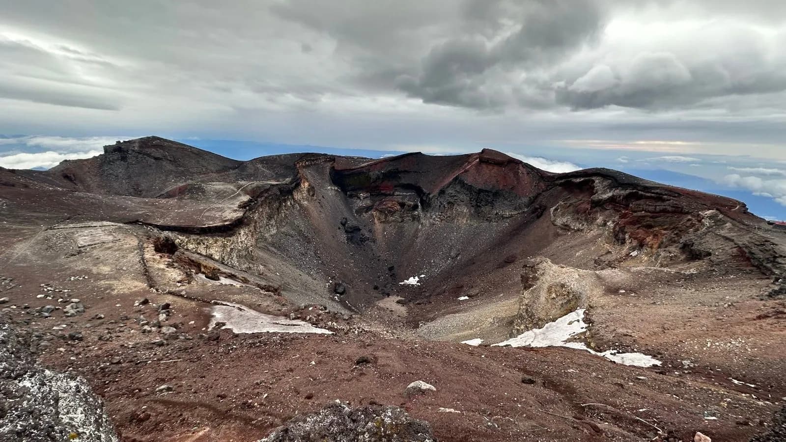 Volcanic crater rim with barren brown and black rock under cloudy skies, top of Mt Fuji.