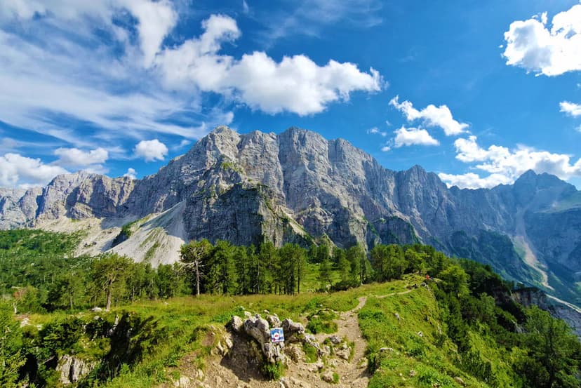 Hiking trail leading toward Slemenova Špica mountain peaks in the Julian Alps under a blue sky.