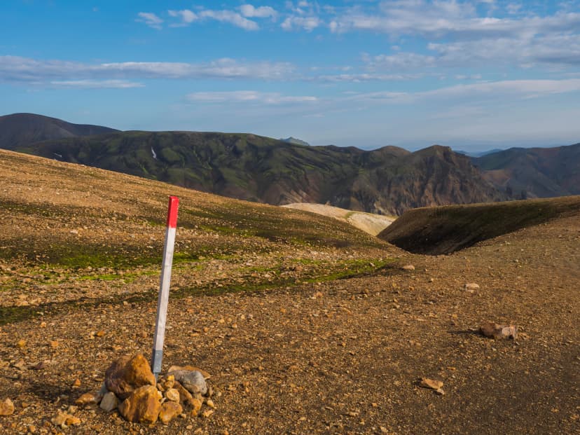 Red mark on trail sign pole on famous Laugavegur hiking trail with Colorful Rhyolit Landmannalaugar mountain at Fjallabak Nature Reserve in Highlands of Iceland
