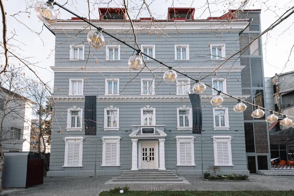 Gray multi-story building with white trim and string lights hanging in the foreground.