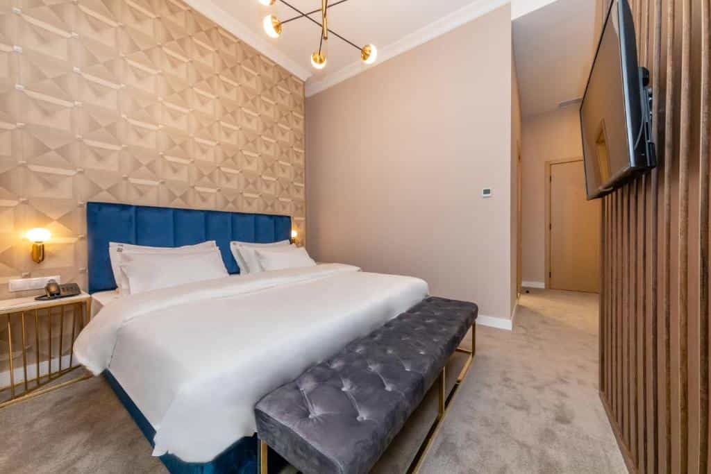 Modern hotel bedroom with blue velvet headboard, white bedding, and geometric patterned accent wall.