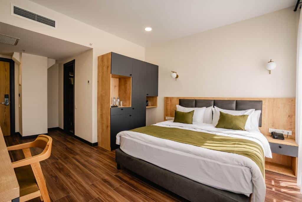 Modern hotel room with a queen-sized bed, olive green accents, and wooden furniture.