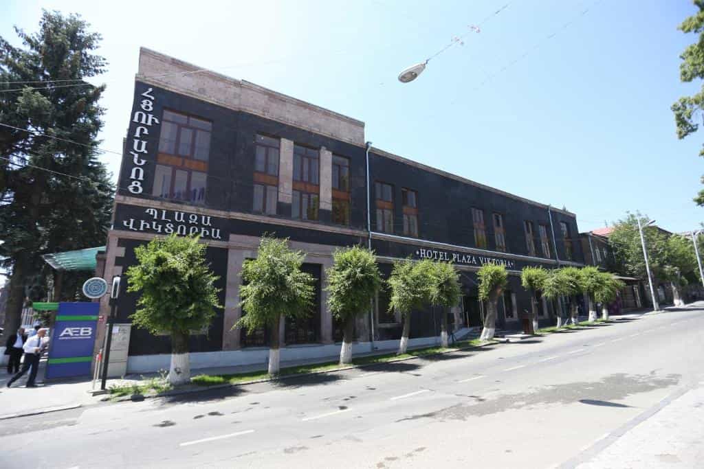 Hotel Plaza Viktoria building exterior with dark stone facade and trees along a street.