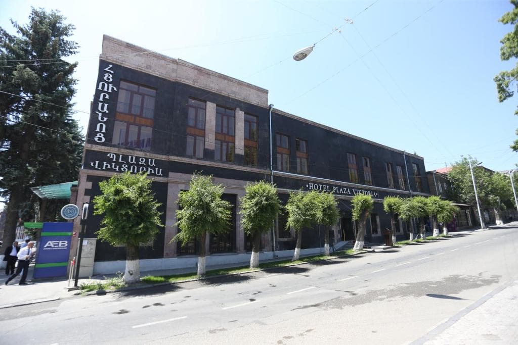 Hotel Plaza Viktoria building exterior with dark stone facade and trees along a street.