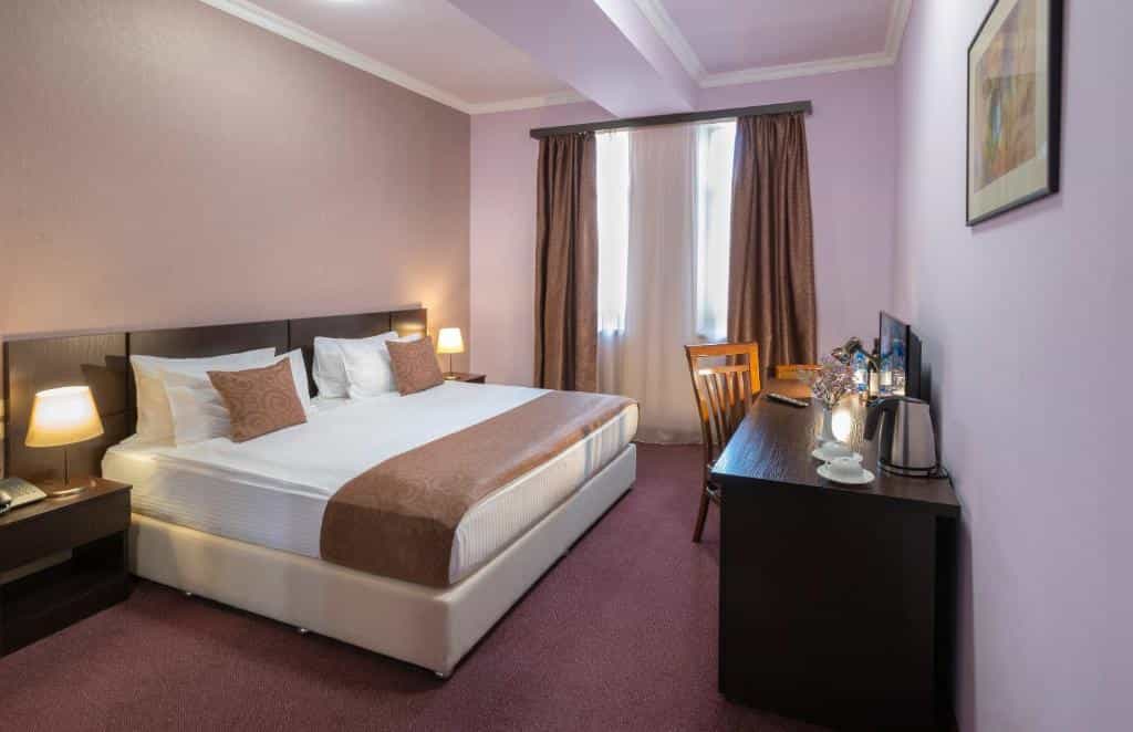 Hotel room with a large bed, desk, chair, and lamps in a room with purple walls.