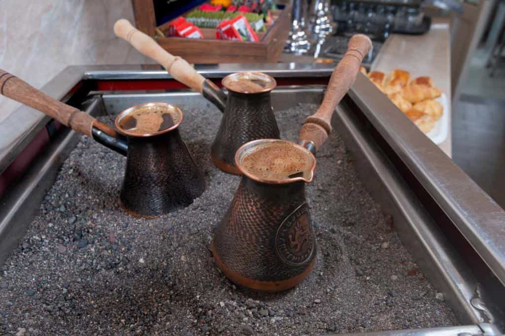 Copper coffee pots brewing in hot sand.