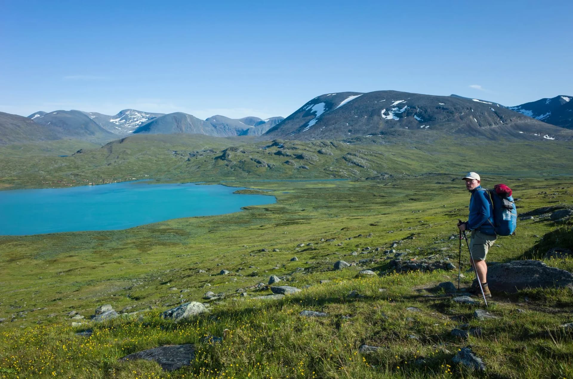 Hiking in Swedish Lapland. Man traveler trekking alone Nordkalottruta Arctic Trail with view of Lake Alisjavri in northern Sweden. Mountain nature of Scandinavia in summer sunny day