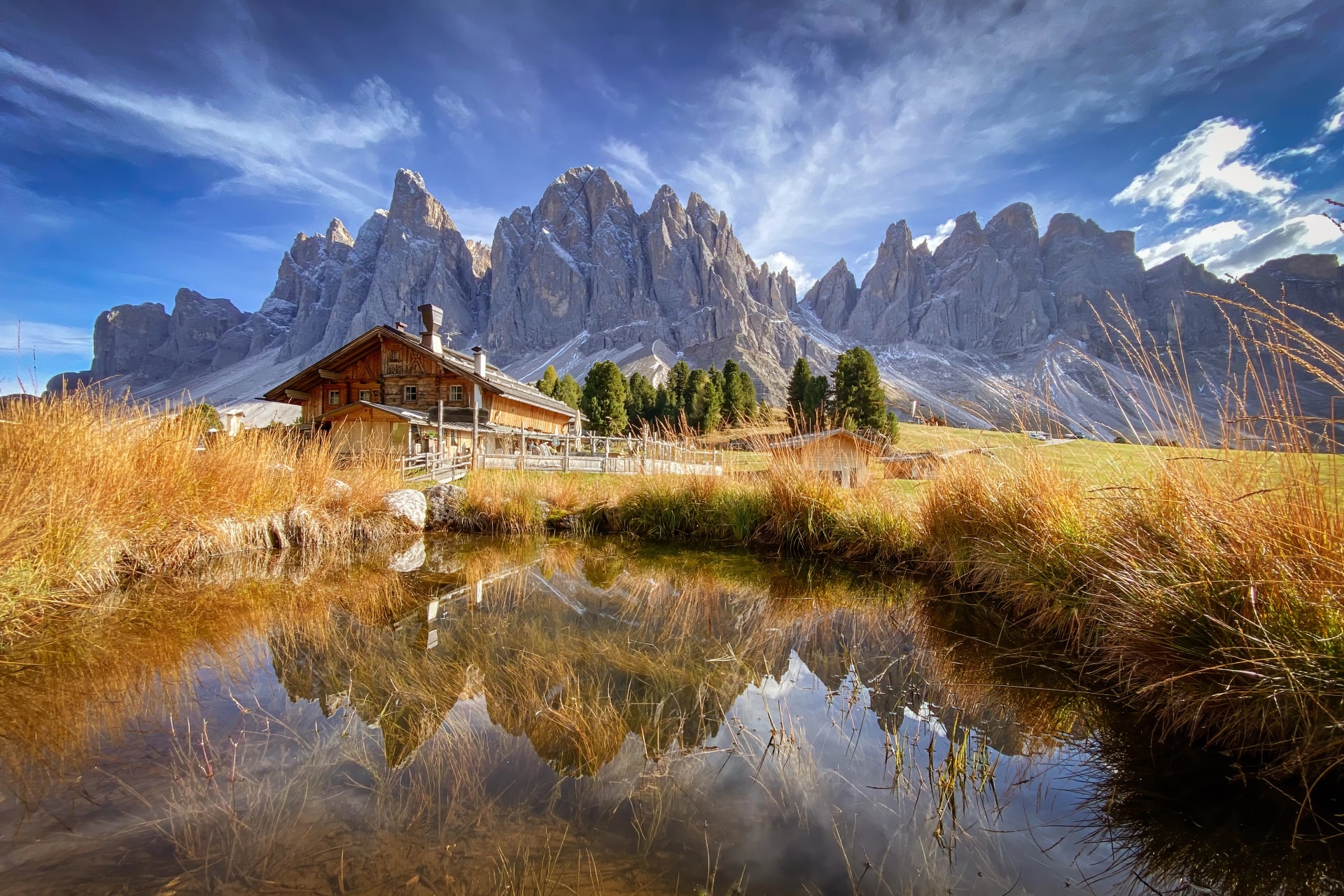 Scenický pohled na Geisler Alm Rifugio delle Odle před dolomitskými horami a odrazem ve vodě rybníka, Jižní Tyrolsko, Itálie