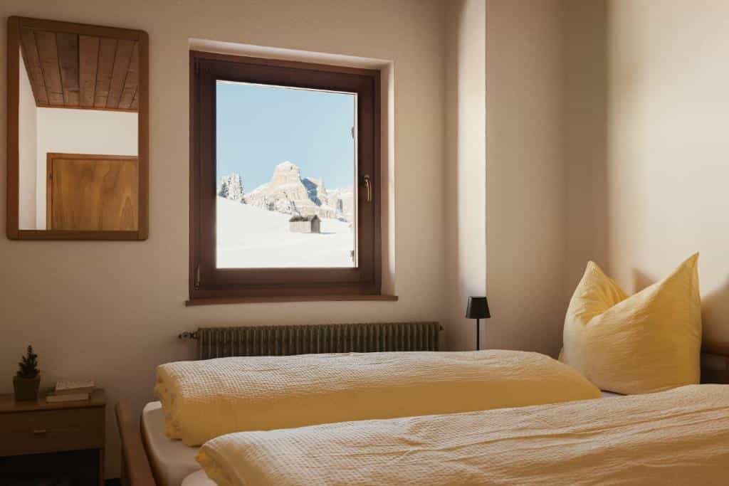 Hotel room with a window view of snow-covered mountain peaks and a small wooden hut.