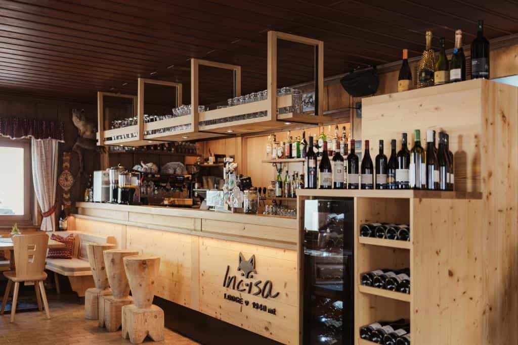 Wooden bar counter with wine bottles and stools inside Incisa Lodge at 1940 meters.