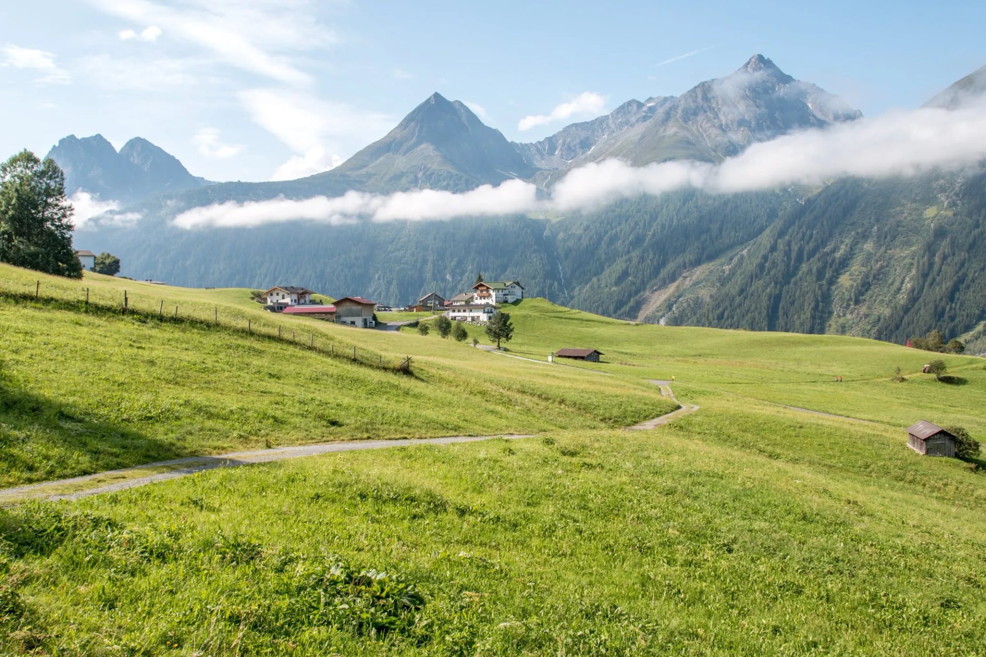 Green pasture and a track below cloud-topped peaks in the Ötztal