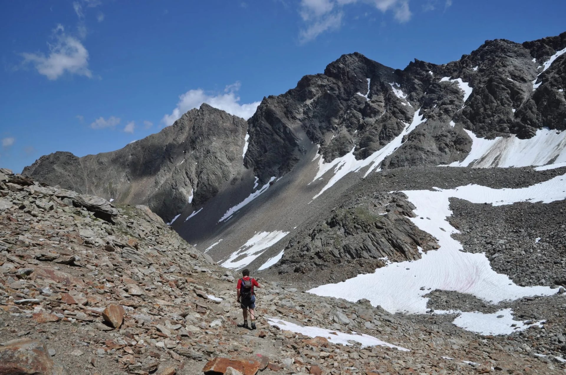 A walker crossing scree below a snow-streaked rock face