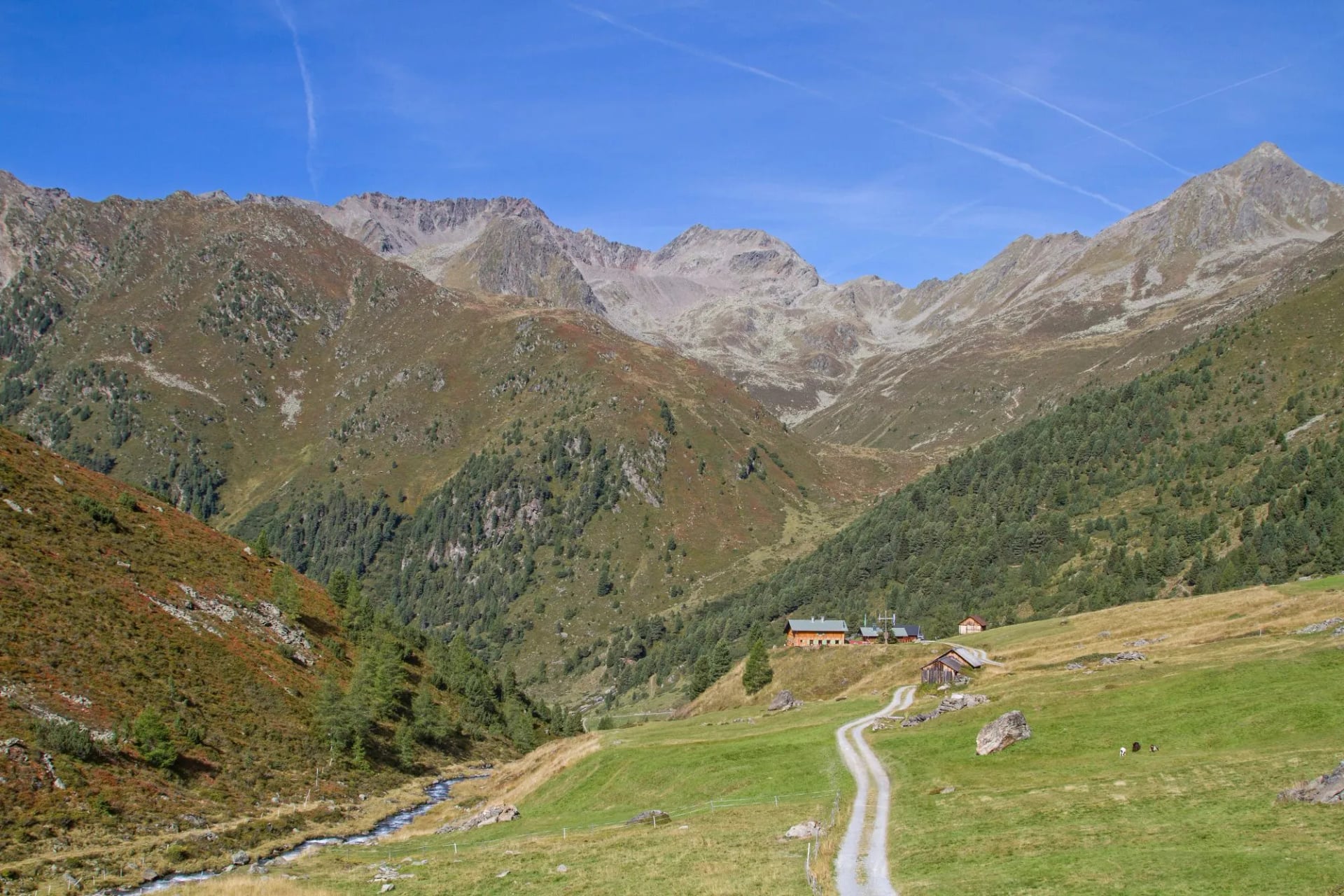 A mountain hut in a green valley below rocky peaks