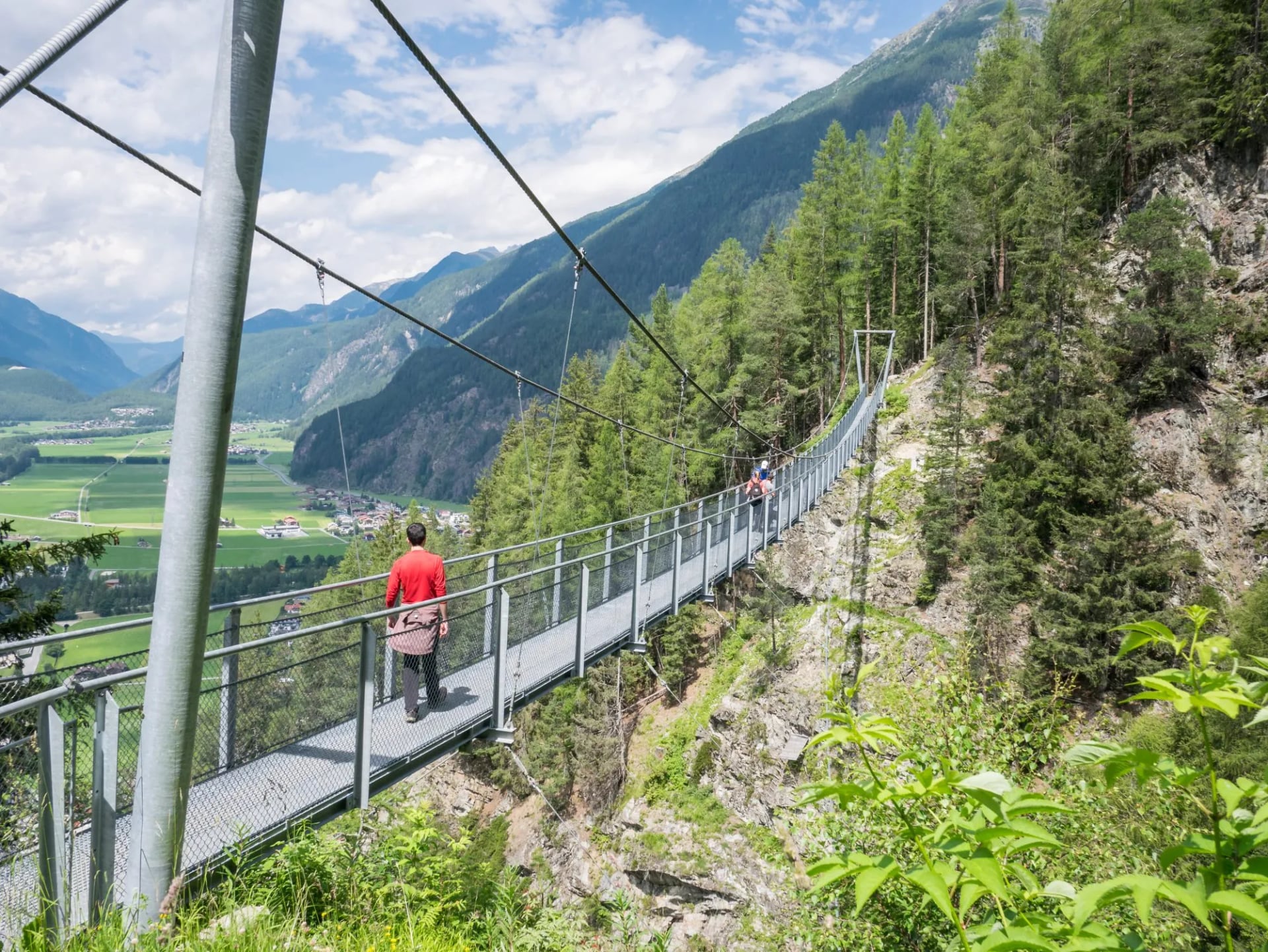 A walker crossing a suspension bridge above the Ötztal valley