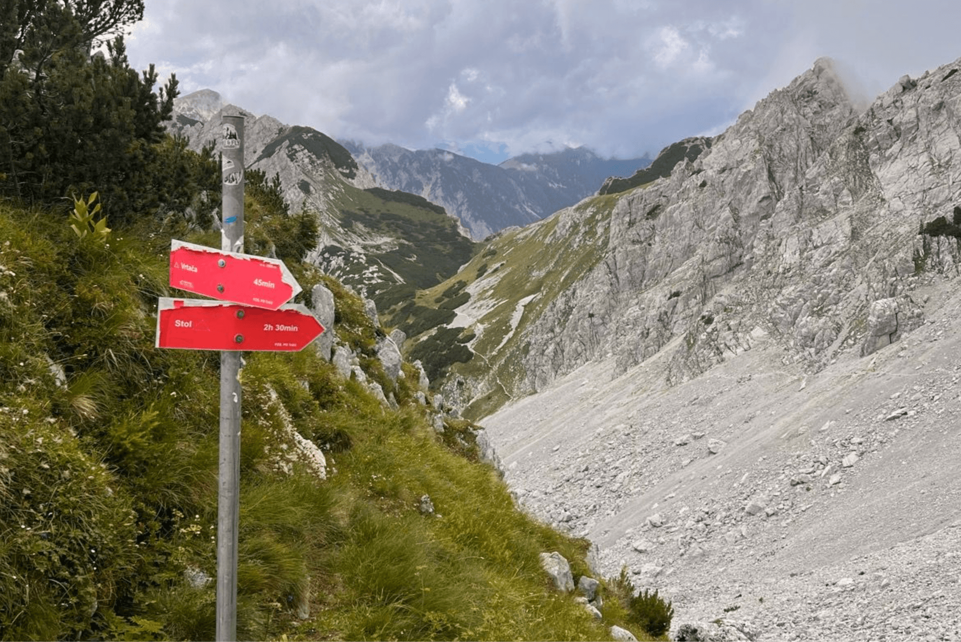 Red hiking trail signpost pointing toward Vrtača and Stol in the Karawanks mountain range.