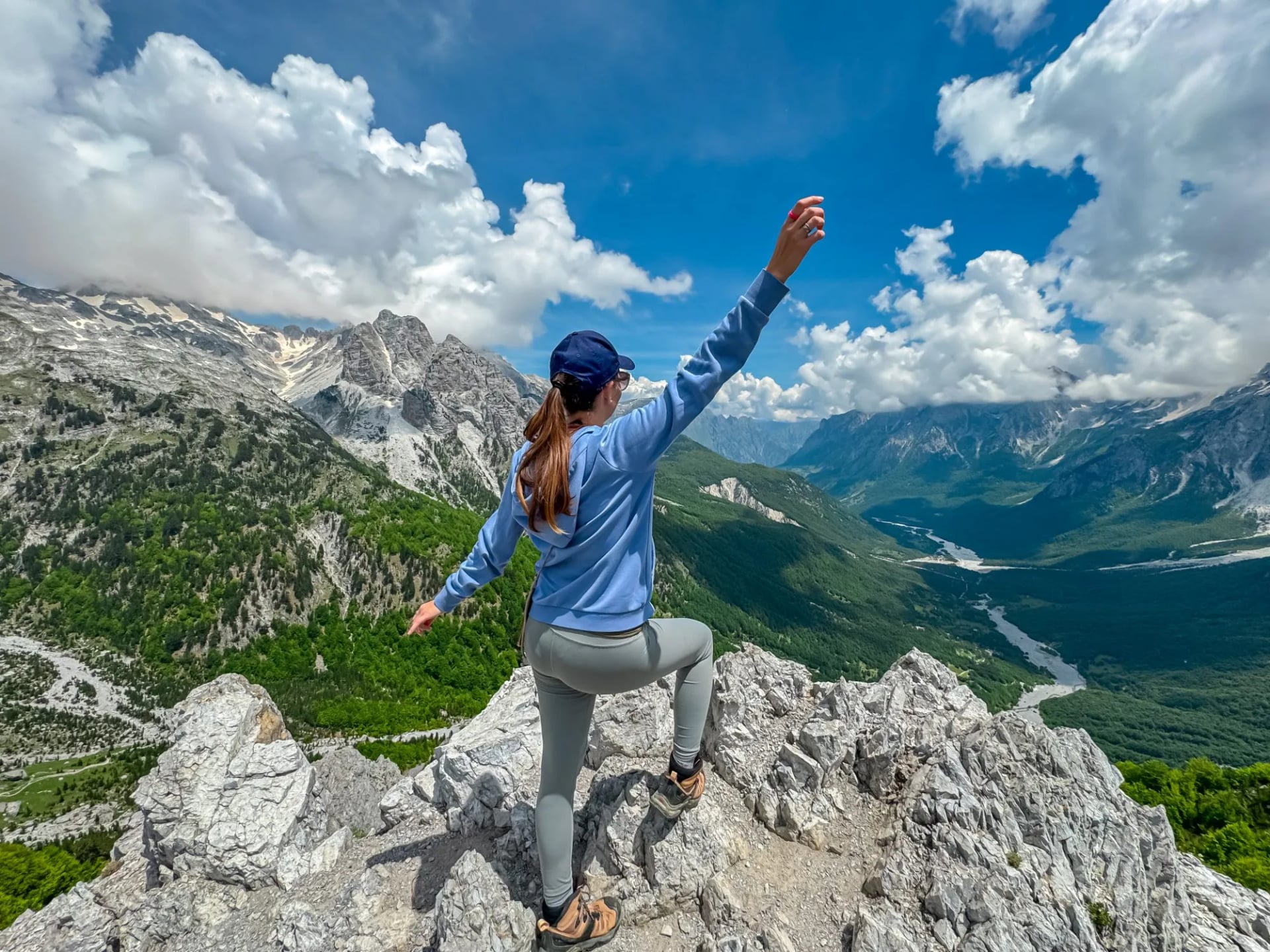 Hiker woman stands on edge of rock formation with panoramic view of Valbona Valley National park surrounded by majestic steep mountain ridges of Albanian Alps (Accursed Mountains), Albania. Wanderlust