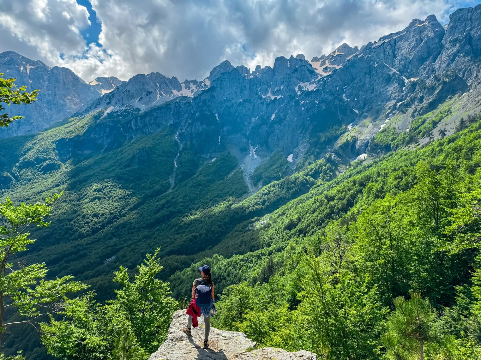 Hiker woman stands on edge of rock formation with panoramic view of Valbona Valley National park surrounded by majestic steep mountain ridges of Albanian Alps (Accursed Mountains), Albania. Wanderlust