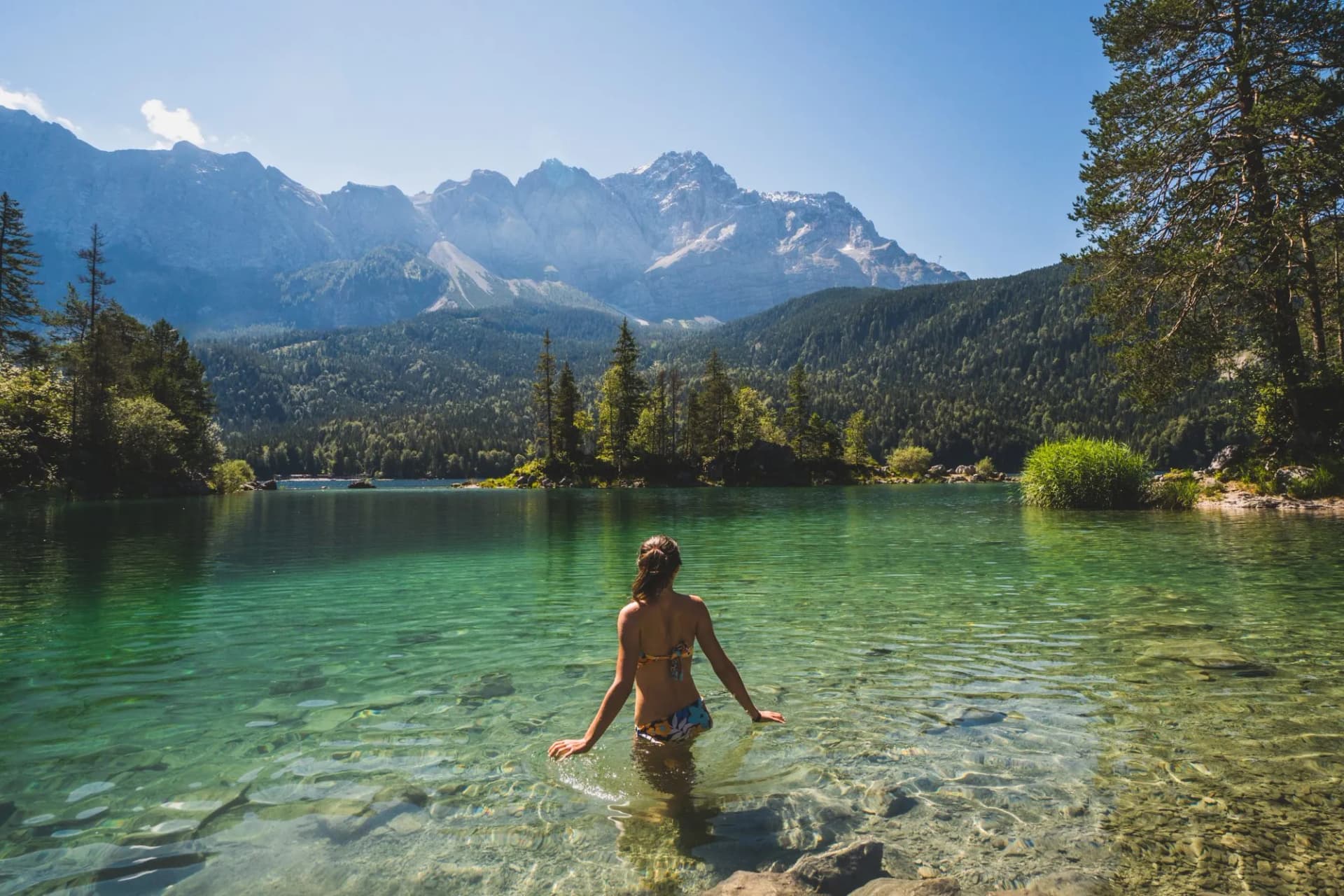 Girl in swimming suite with the back at the camera swimming in a beautiful mountain lake, in the Bavarian Alps